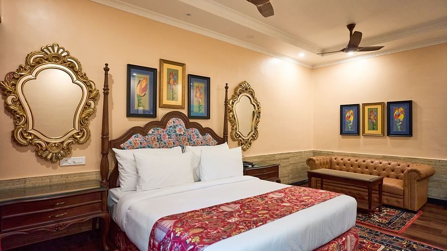 A spacious room with a large bed on one side and cushioned seating furniture on the other, adorned with wall-mounted frames for decoration at Mayfair Manor, Alibag