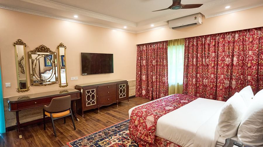 A spacious room featuring a dressing table with an adjacent mirror, a wall-mounted TV above a wooden table, captured from a bedside perspective at Mayfair Manor, Alibag