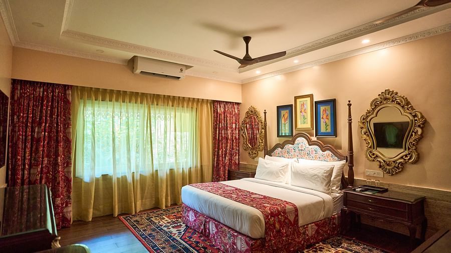 A spacious room featuring a large bed, wooden bedside tables, and windows draped with curtains at Mayfair Manor, Alibag