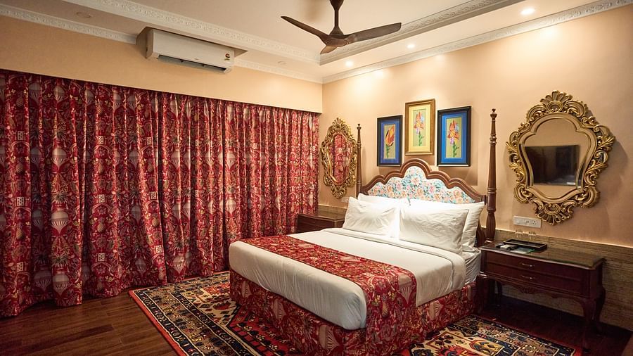 A spacious room featuring a large bed, wooden bedside tables, and windows draped with curtains at Mayfair Manor, Alibag