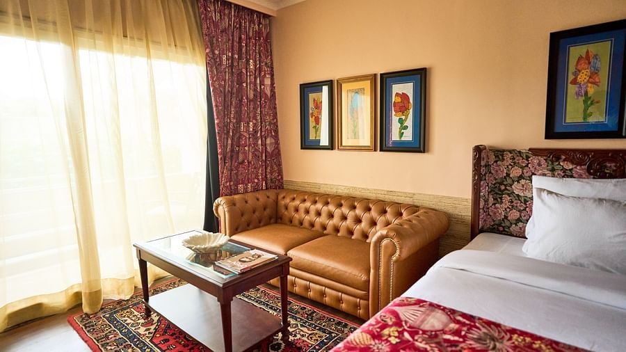 A spacious room featuring a bed on one side, a cushioned sofa on the other, and a glass table near the window adorned with closed curtains at Mayfair Manor, Alibag