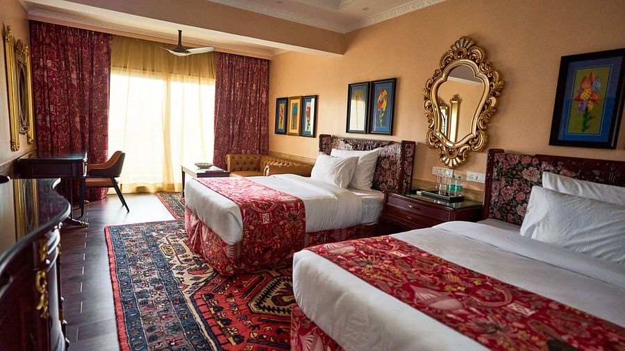 Side view of a spacious room featuring a double bed, wall-mounted frames for decoration, and windows elegantly covered with curtains at Mayfair Manor, Alibag