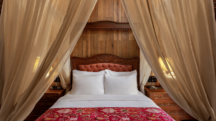 Elegant suite bedroom with a draped canopy bed and red patterned bedspread at Mayfair Manor, Jungpana.