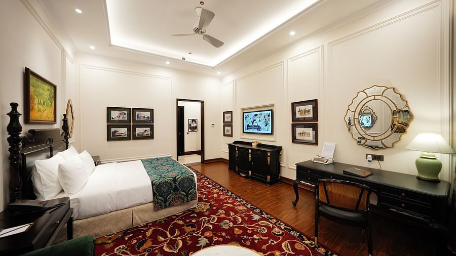 a king size bed facing a workstation in a room whose walls are decorated with paintings - Mayfair Tea Resort, Siliguri 