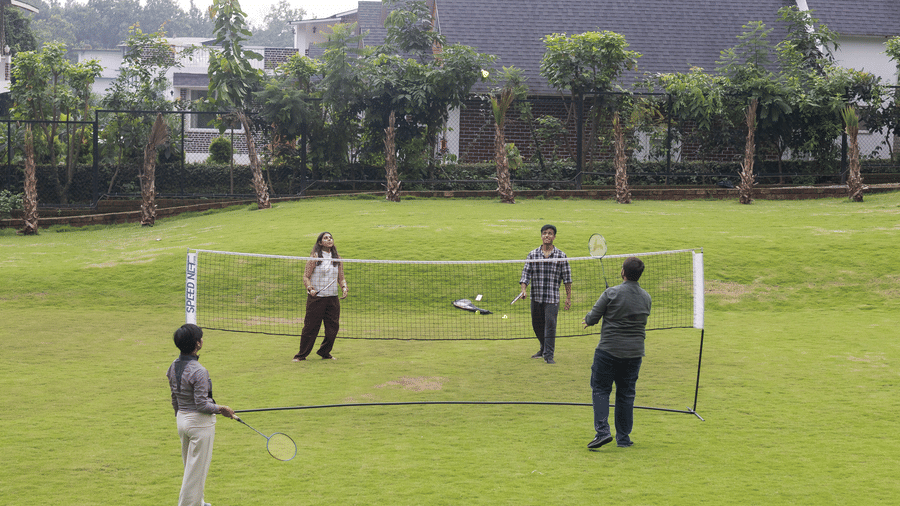 A group of people playing badminton on a sunny afternoon, with the resort’s lush lawns in the background - Megha Resort & Villas, Dehradun