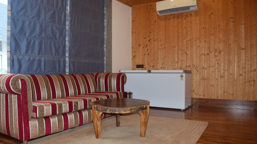 A spacious room with wooden flooring, a bed, and an ironing board near a window with curtains is present - Megha Resort & Villas, Dehradun