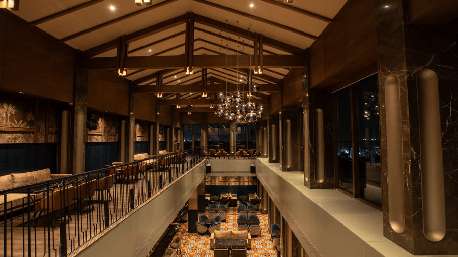 Long indoor bar space with seating, railings, and ceiling lights at Origyn, Merlis Hotel, Coimbatore.