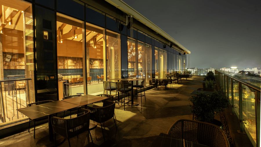 Outdoor seating area with tables, chairs, and city lights view at Origyn Bar in Coimbatore | Merlis Hotel