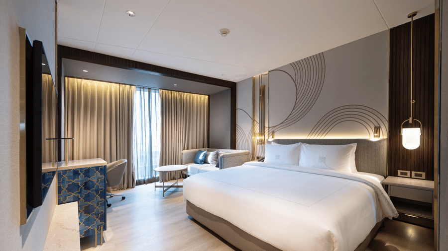 A hotel accommodation in Coimbatore featuring a plush bed facing the TV on the wall and a large ceiling-to-floor window covered with curtains at Merlis Hotel, Coimbatore