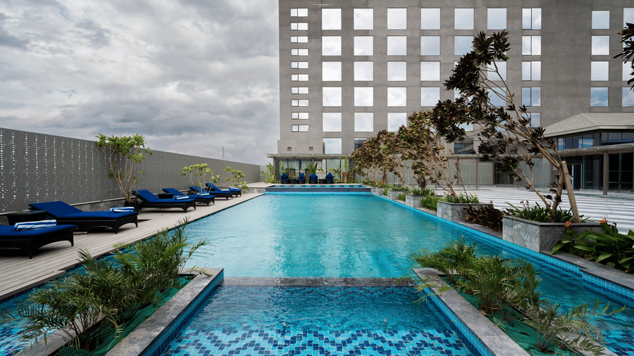 Outdoor swimming pool with city view, stylish lounge chairs, and potted plants at Merlis Hotel, Coimbatore - a  swimming pool hotel in Coimbatore.
