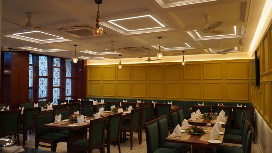 A wide shot of a dining hall with multiple tables set for a meal. The walls are yellow, and the chairs are dark green.