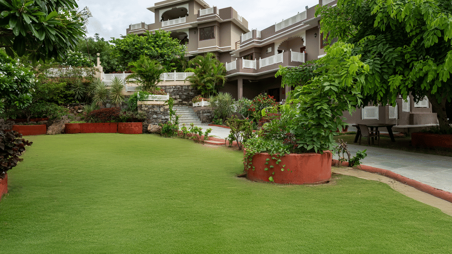 A manicured green lawn surrounds a multi-storey hotel property framed by lush tropical trees.