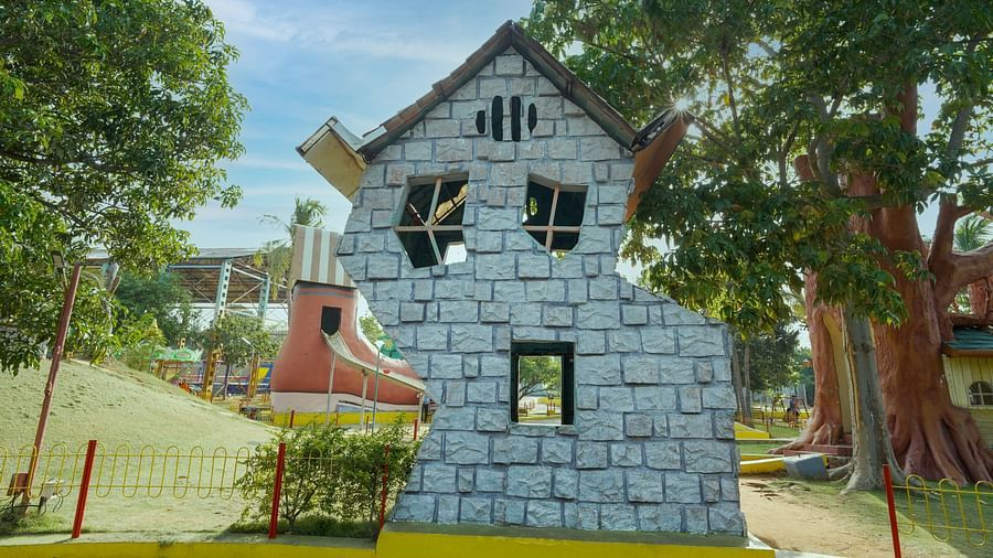 A playful, two-storied house facade built at MGM Dizzee World featuring stone blocks, set against a backdrop of trees and a bright sky.
