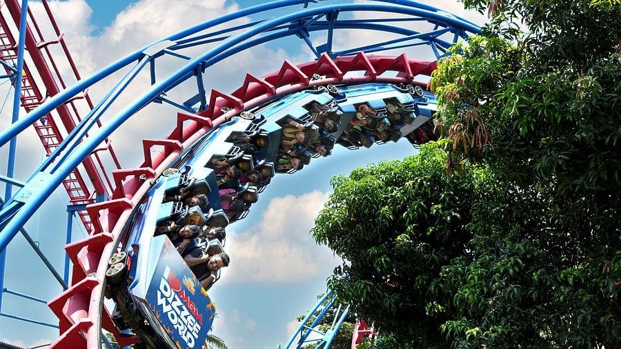 A part of roller coaster ride where people are seating and the ride is upside down with a backdrop of trees at MGM Dizzee World.