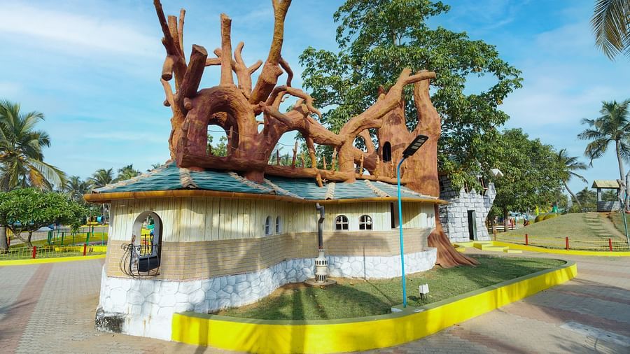 A whimsical, multi-storied building with a tree-like sculpture on top at MGM Dizzee World, standing in a lush green field under a clear blue sky.