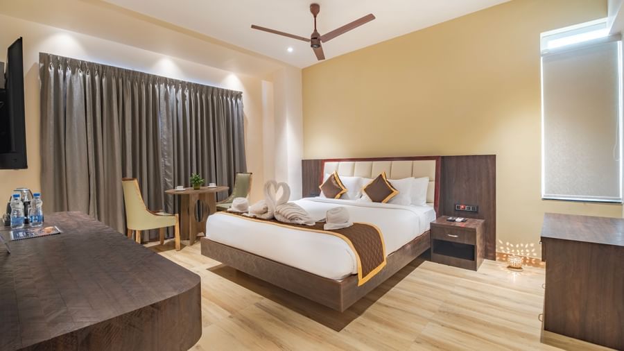 Spacious room at Monday Hotels Amalapuram Heights with warm lighting, ceiling fan, bed-side table, and a seating area.