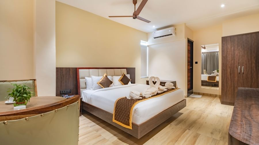 Spacious room at Monday Hotels Amalapuram Heights with double bed, ceiling fan, mirror, and air-conditioning.