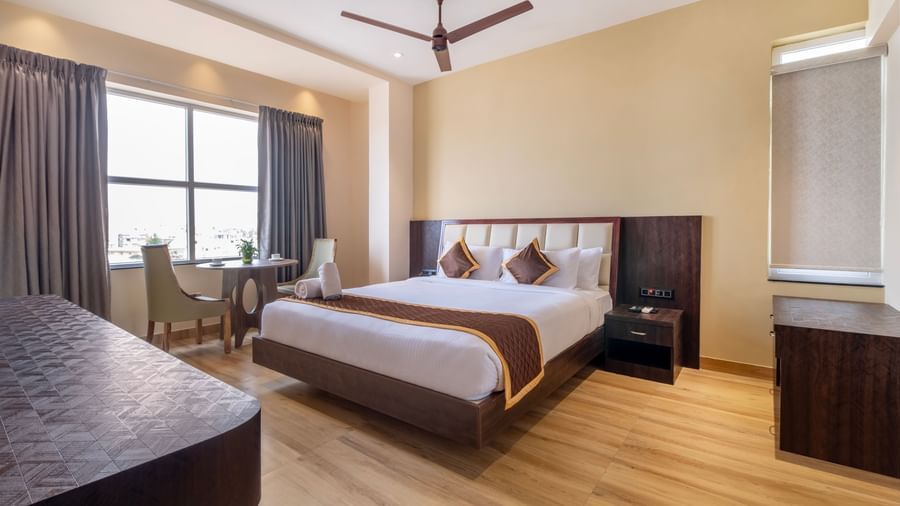Spacious room at Monday Hotels Amalapuram Heights with king bed, ceiling fan, seating area, and a window view.