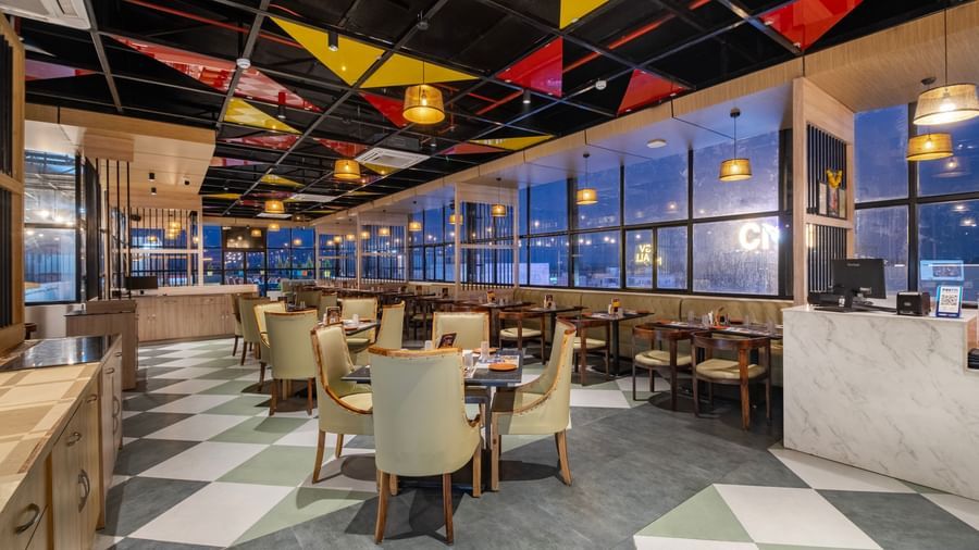 Restaurant at Monday Hotels Amalapuram Heights with colourful ceiling decor, city view, and neatly arranged tables and chair.