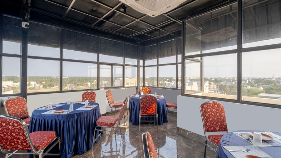 Glass-walled banquet area at Monday Hotels Amalapuram Heights with city view and cluster seating arrangement.