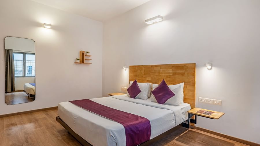 A hotel room with a double bed, wooden flooring, a large mirror and a side table - Monday Hotels HITEC City, Hyderabad