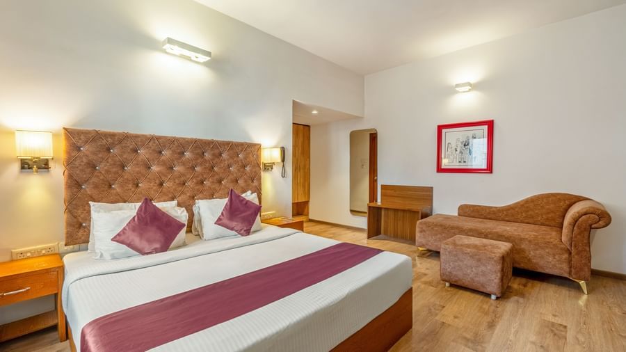 A hotel room with a double bed, a cushioned sofa, and a wooden desk placed beside the bed - Monday Hotels HITEC City, Hyderabad