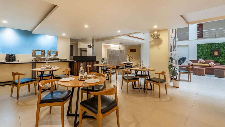 A large dining space with wooden tables, chairs, and an open kitchen view - Monday Hotels HITEC City, Hyderabad