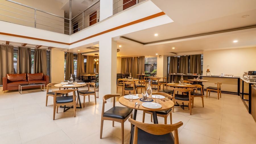 A dining area with multiple tables and chairs arranged neatly and a seating area with a cushioned sofa - Monday Hotels HITEC City, Hyderabad