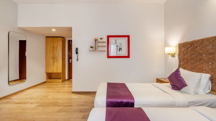 A spacious hotel room with 2 single beds, a frame, a mirror attached to the wall and a wall-mounted light – Monday Hotels HITEC City, Hyderabad