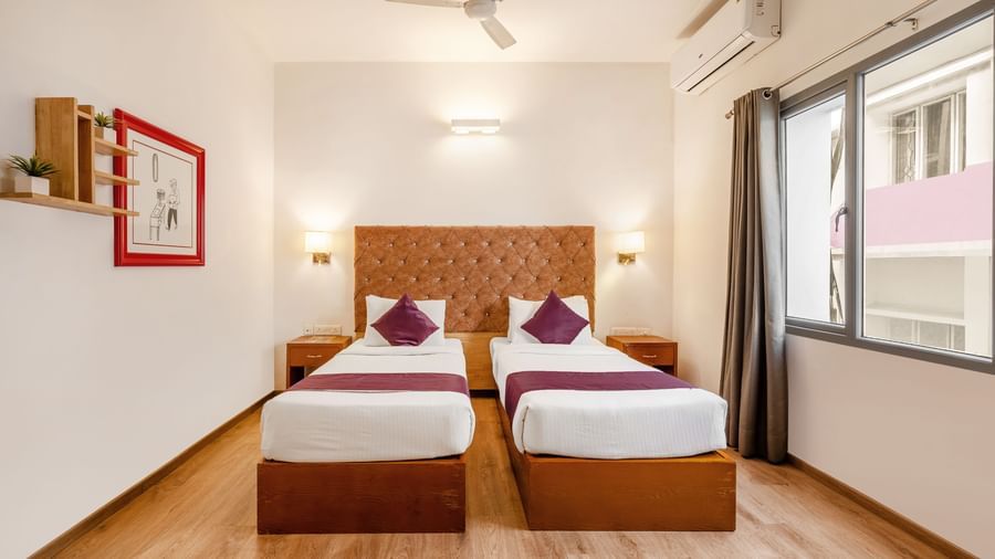 A hotel room with 2 single beds. a ceiling fan and a large window with the curtains opened - Monday Hotels HITEC City, Hyderabad