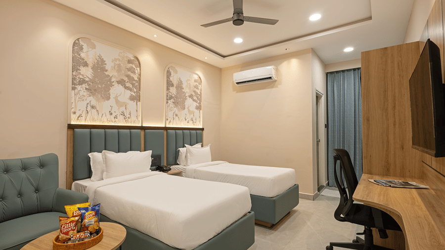 Deluxe room with twin beds, deer and forest murals, green armchair, snack basket, curved work desk and TV at Monday Hotels & Suites Madhapur, Hyderabad.