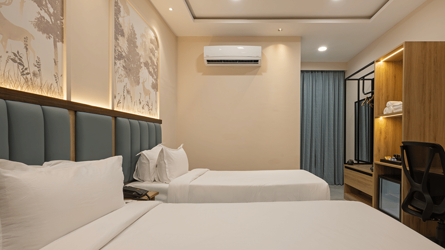 Twin beds with green padded headboards, deer mural, wardrobe unit and curtained window in a Deluxe room at Monday Hotels & Suites Madhapur, Hyderabad.