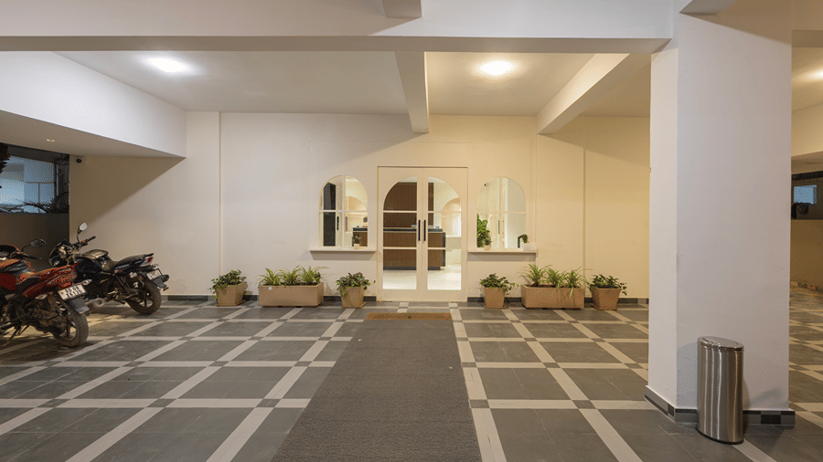 Covered entrance porch with glass double doors, arched windows, planters, parked motorcycles and floor mat at Monday Hotels & Suites Madhapur, Hyderabad.