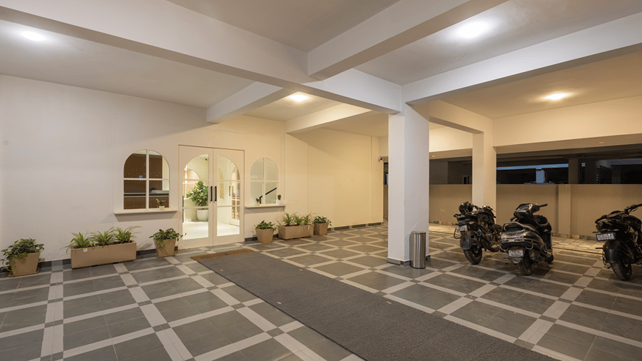 Covered entrance porch with arched glass doors, planters, a floor mat and parked 2-wheelers at Monday Hotels & Suites Madhapur, Hyderabad.