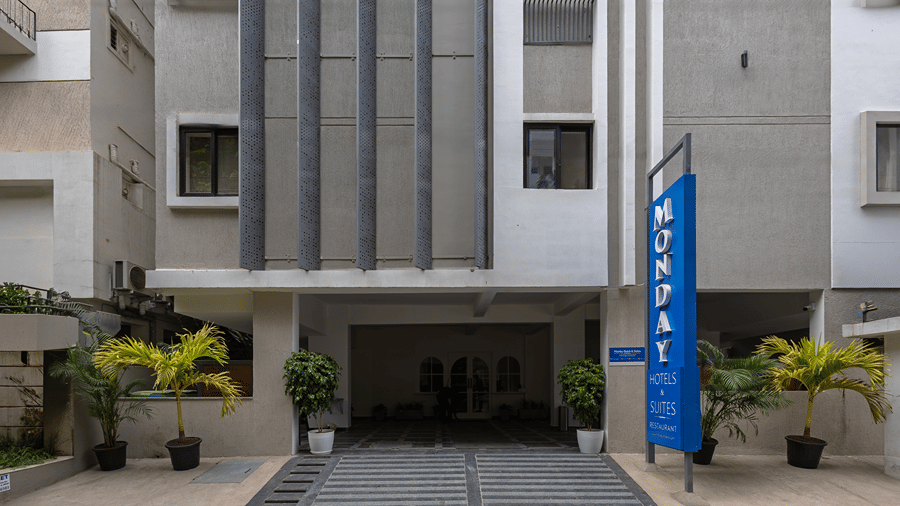 Entrance driveway with steps, potted palms, a covered porch with arched doors and a blue vertical hotel sign at Monday Hotels & Suites Madhapur, Hyderabad.