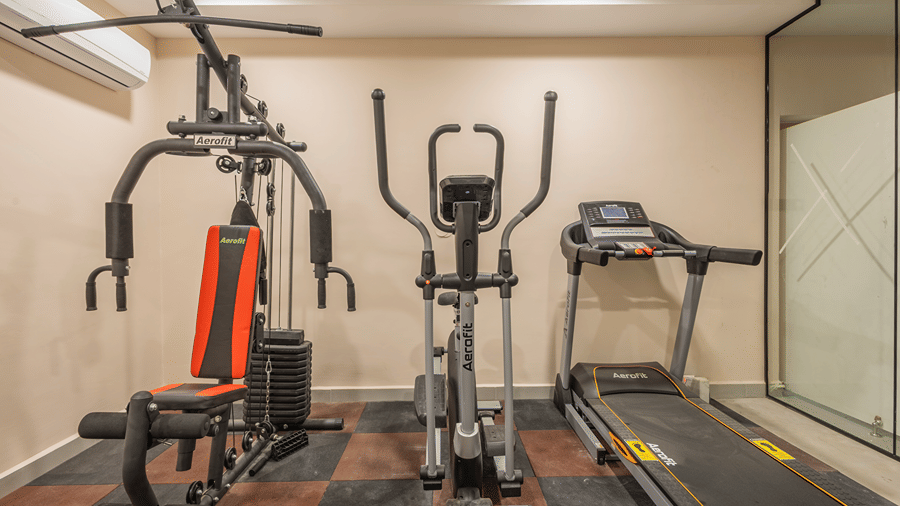 Multi-gym station, elliptical trainer and treadmill beside a glass partition in the fitness centre at Monday Hotels & Suites Madhapur, Hyderabad.