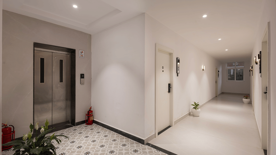 Guest corridor with room doors, wall lights and potted plants beside the lift and patterned floor at Monday Hotels & Suites Madhapur, Hyderabad.