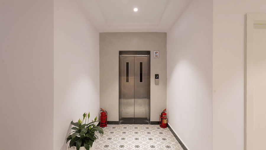 Lift lobby with stainless-steel lift doors, fire extinguishers, a potted plant and patterned floor tiles at Monday Hotels & Suites Madhapur, Hyderabad.