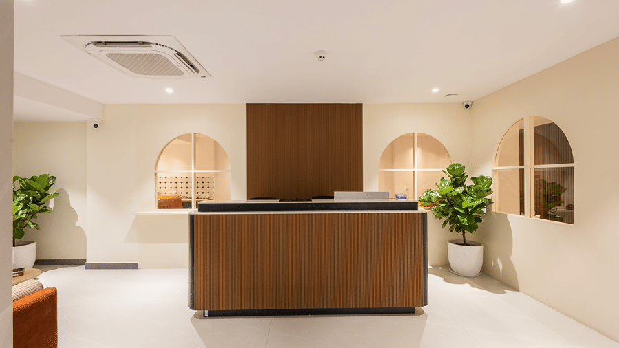 Reception desk with wooden panelling, arched windows and potted fiddle-leaf figs in the lobby at Monday Hotels & Suites Madhapur, Hyderabad.