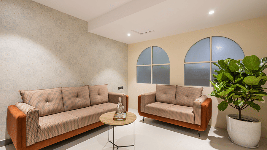 Lobby seating with 2 sofas, a round coffee table, arched frosted windows and a potted fiddle-leaf fig at Monday Hotels & Suites Madhapur, Hyderabad.