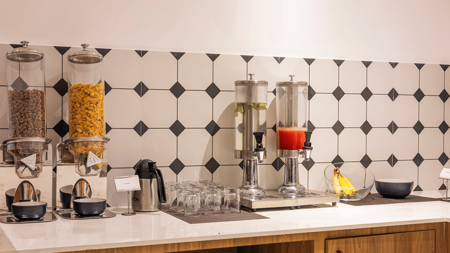 Cereal dispensers, infused water and juice dispensers, glasses, a flask and bananas on the buffet at M-Salt at Monday Hotels & Suites Madhapur, Hyderabad.