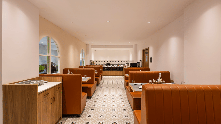 M-Salt restaurant with tan leather booths, set tables, arched windows and the buffet counter at the far end at Monday Hotels & Suites Madhapur, Hyderabad.
