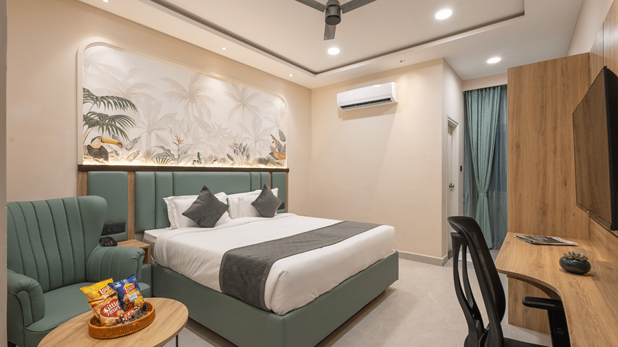 Superior room with a king bed, green padded headboard, tropical bird mural, green armchair, snack basket and work desk at Monday Hotels & Suites Madhapur, Hyderabad.