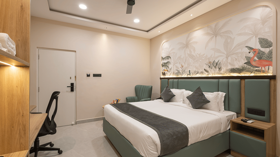 Superior room with a king bed under a flamingo mural, bedside table, work desk with chair and entrance door at Monday Hotels & Suites Madhapur, Hyderabad.