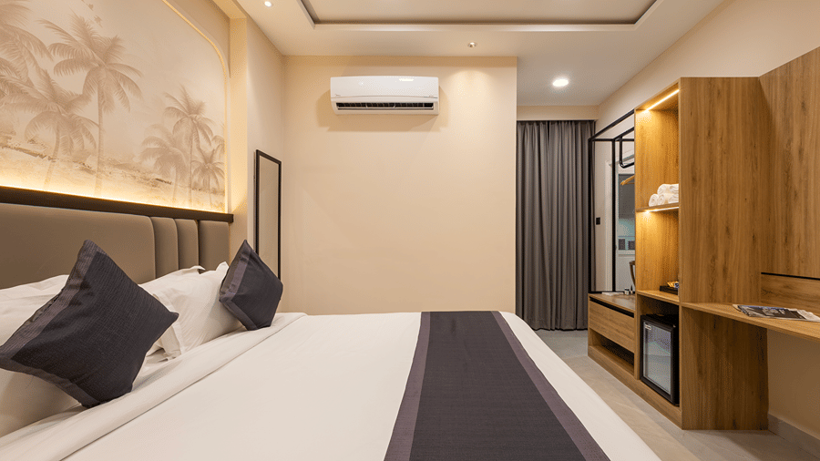 Bed with a navy runner, palm mural, wardrobe unit with minibar and a curtained window in a Premium room at Monday Hotels & Suites Madhapur, Hyderabad.