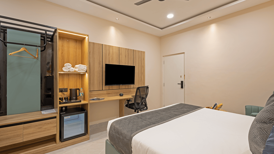 Open wardrobe, towel shelves, kettle, minibar, wall-mounted TV and work desk facing the king bed in a Superior room at Monday Hotels & Suites Madhapur, Hyderabad.