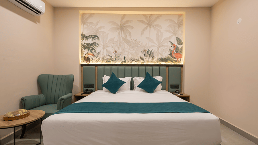 Studio Suite bedroom with a king bed, teal cushions, tropical mural, green armchair and side table with fruit at Monday Hotels & Suites Madhapur, Hyderabad.