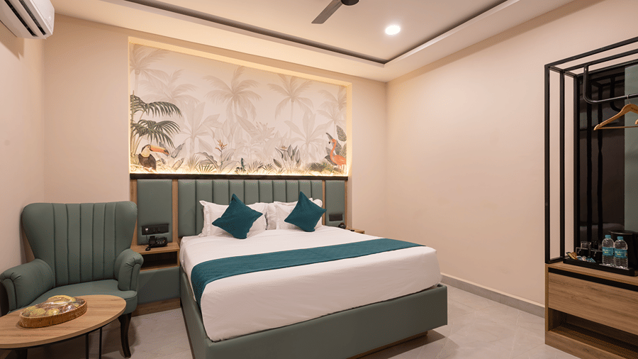 Studio Suite bedroom with a king bed, teal cushions, tropical mural, wingback armchair and open wardrobe at Monday Hotels & Suites Madhapur, Hyderabad.