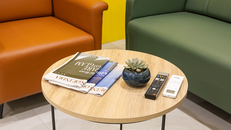 Coffee table with newspapers, a succulent and remotes between tan and green sofas in a Studio Suite at Monday Hotels & Suites Madhapur, Hyderabad.
