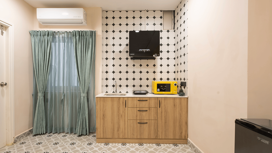 Studio Suite kitchenette with wooden cabinets, sink, induction cooktop, chimney, yellow microwave and fridge at Monday Hotels & Suites Madhapur, Hyderabad.